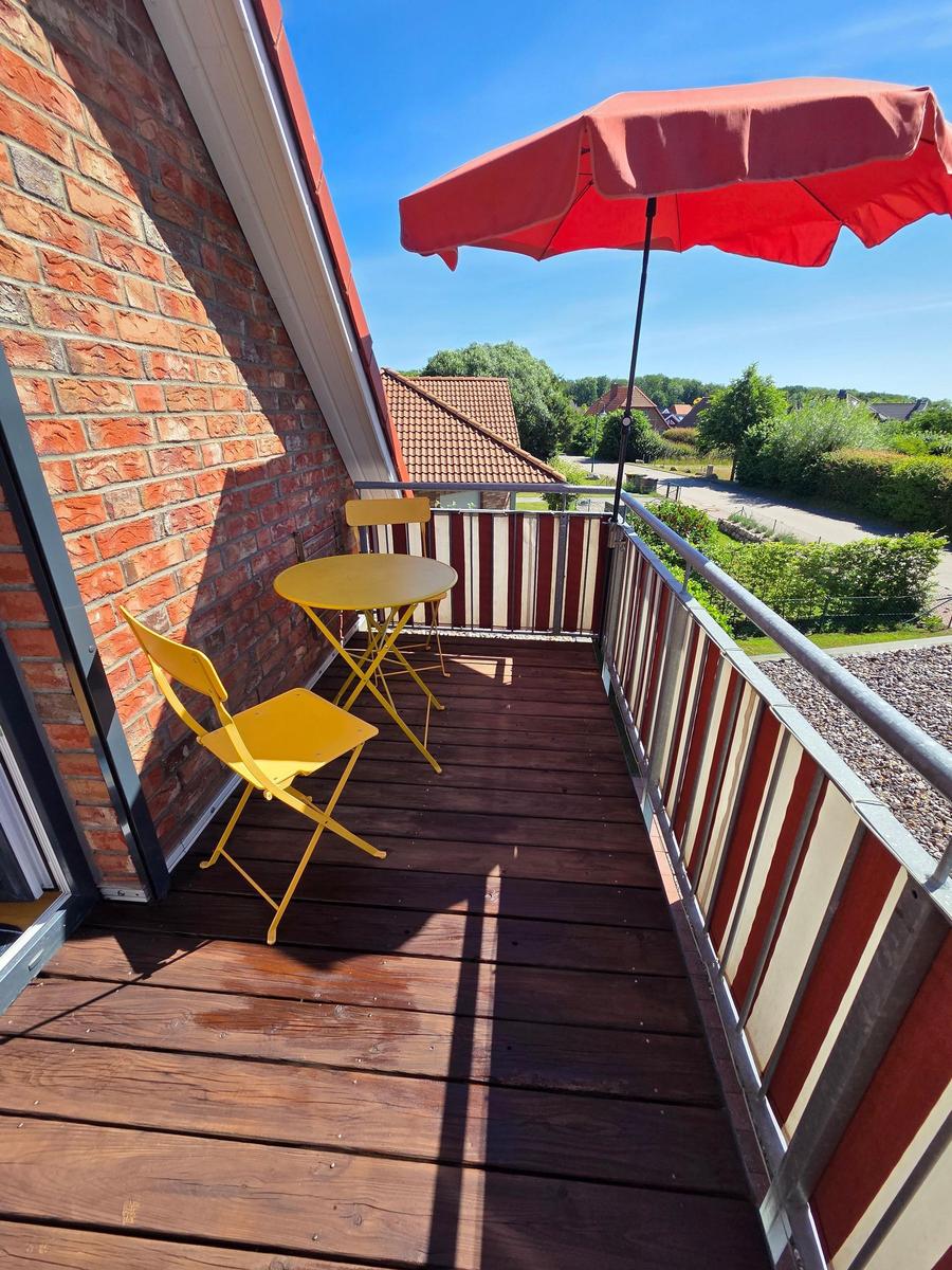 Terrasse mit gelbem Tisch und Stühlen unter rotem Sonnenschirm. Holzdecke und Blick auf Garten.