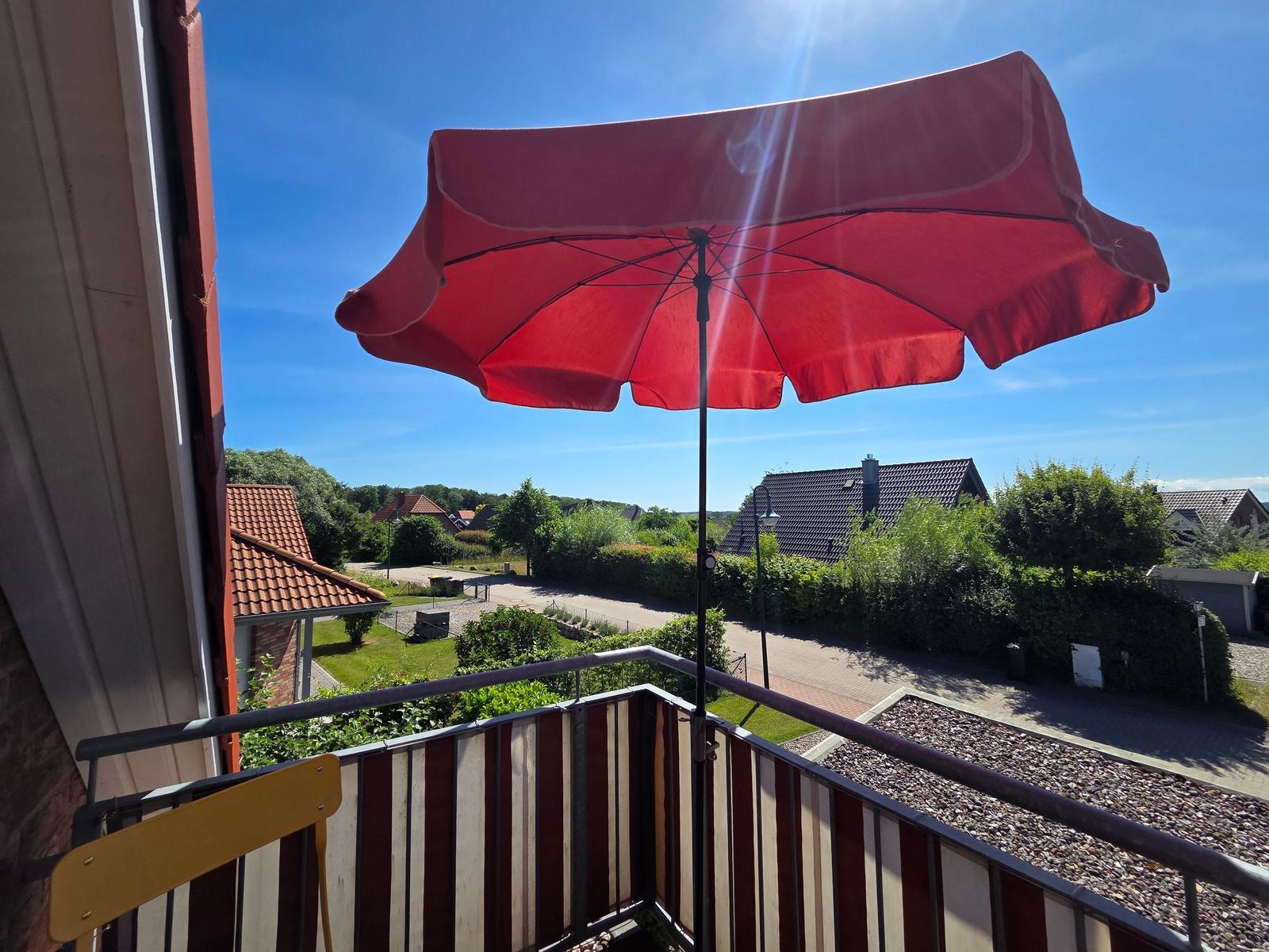 Terrasse mit rotem Sonnenschirm und Blick auf grüne Umgebung und Häuser.