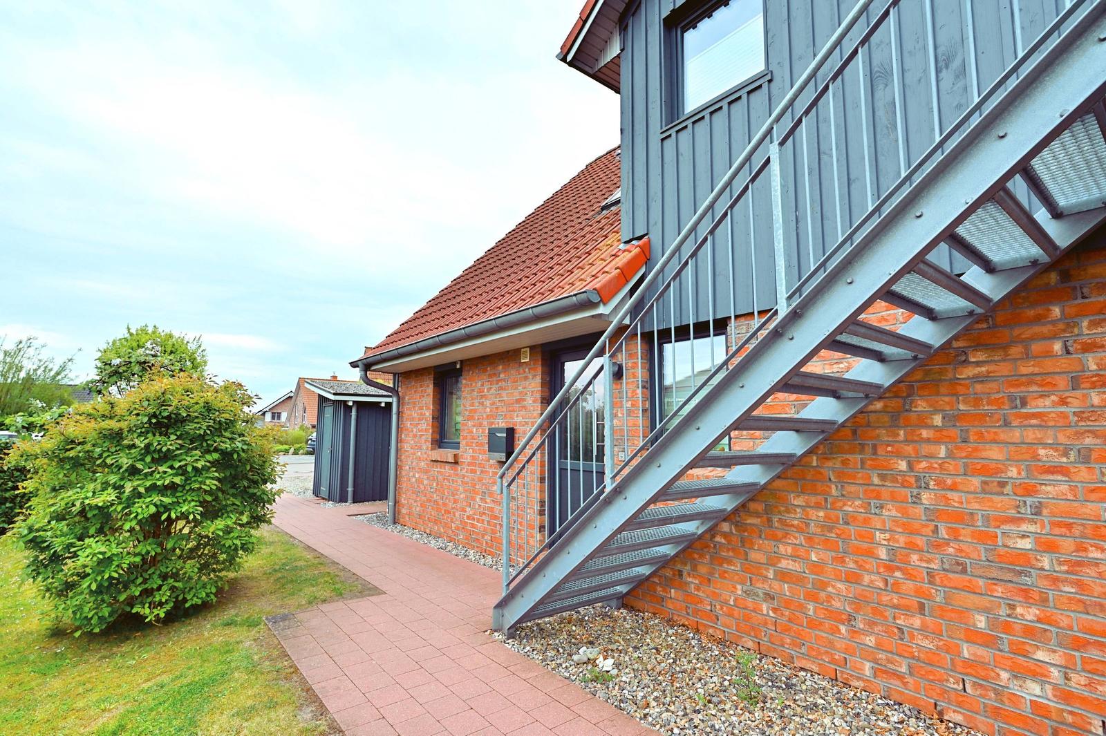 Haus mit rotem Ziegeldach und Metalltreppe an Backsteinmauer.
