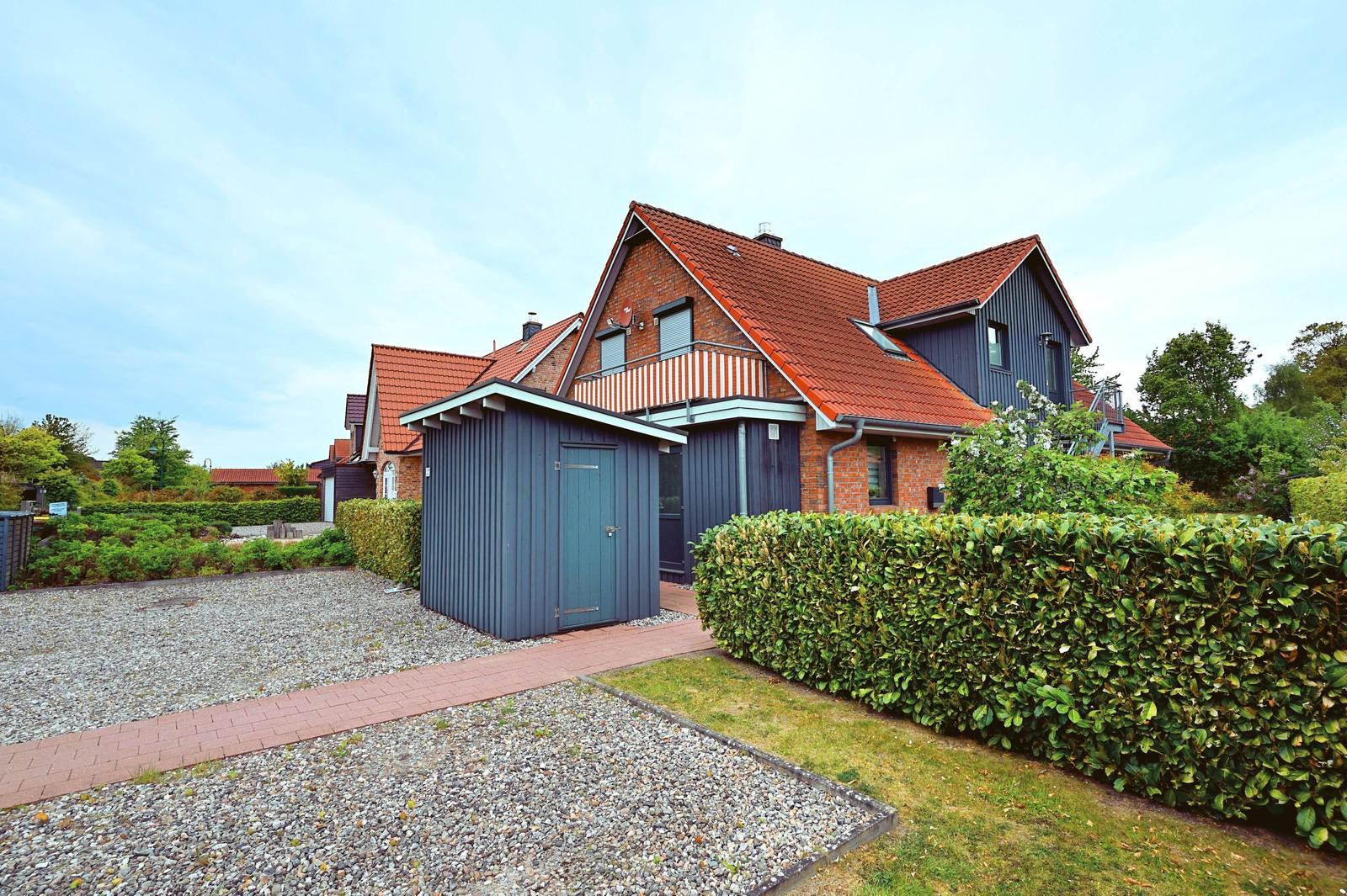 Haus mit rotem Dach und dunkelblauen Wänden, umgeben von Grün und einem Kiesweg.