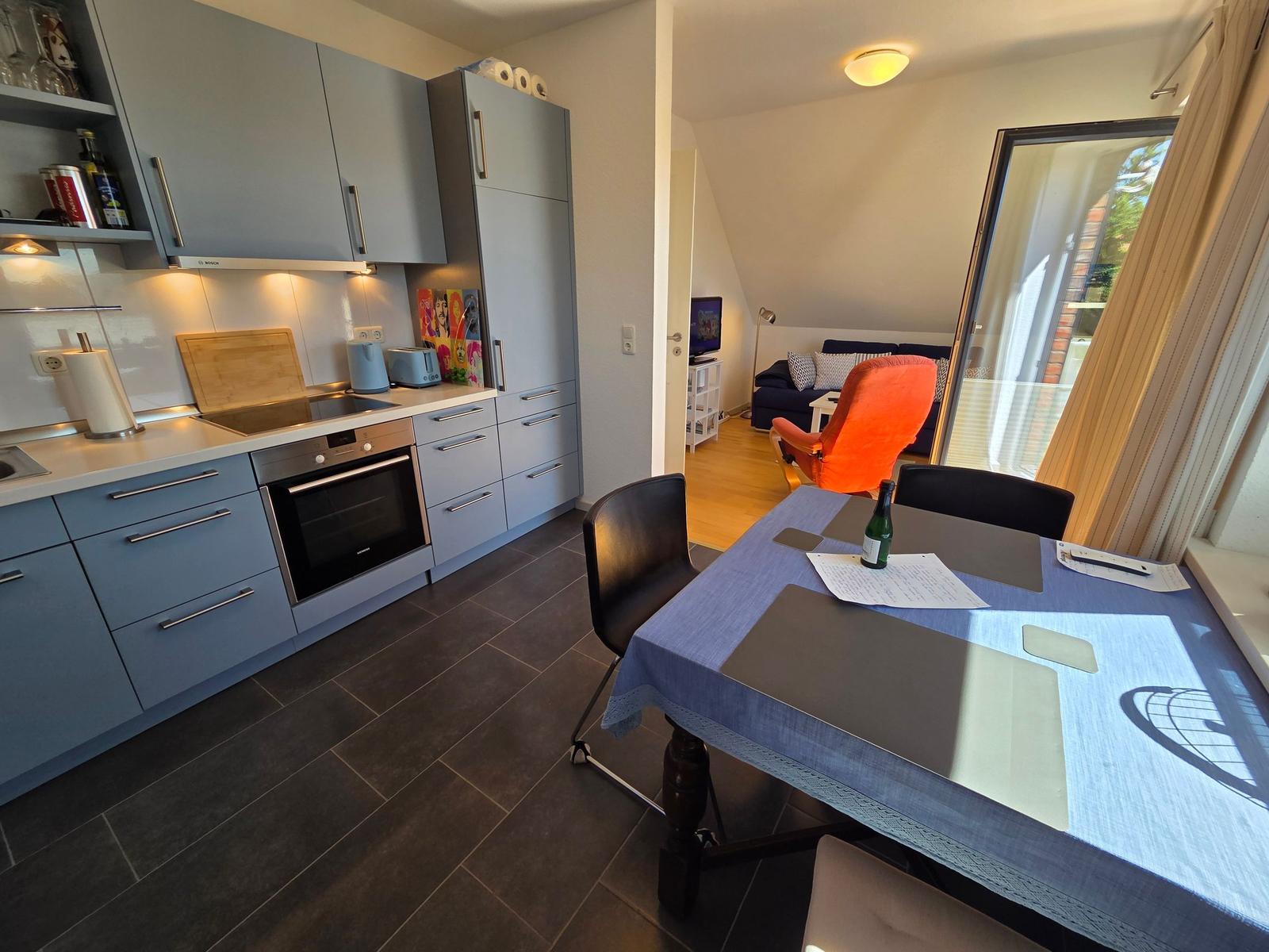 Küche mit Essbereich und Blick in Wohnzimmer mit Sofa und orangefarbener Sitzgelegenheit.