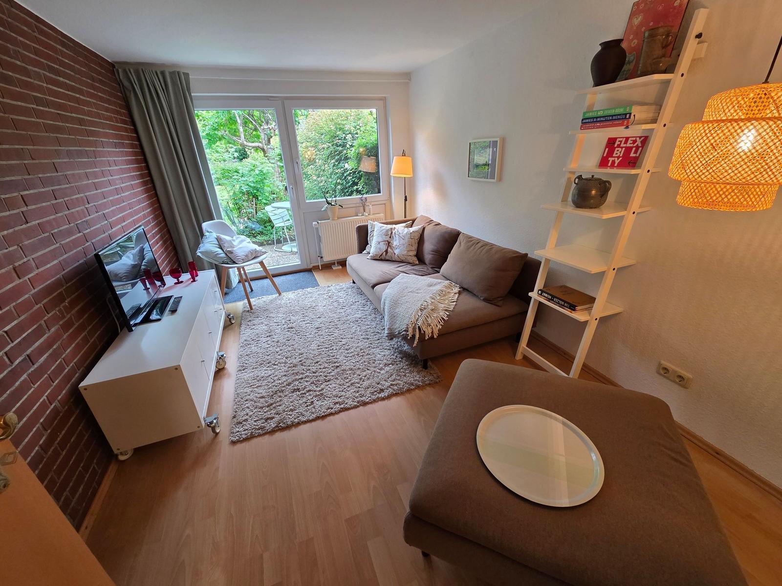 Wohnzimmer mit Sofa, Fernseher und Terrassentür. Holzfußboden und Bücherregal.