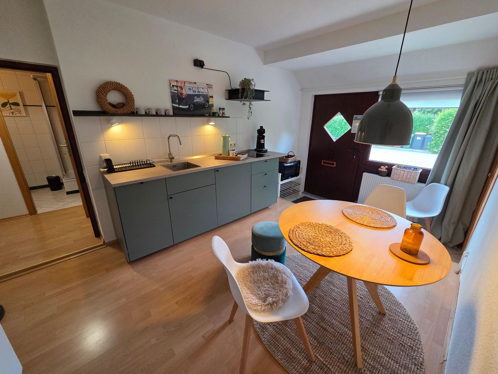 Küche mit Essbereich, Holzboden und Fensterblick. Tisch mit Stühlen und Hängelampe.