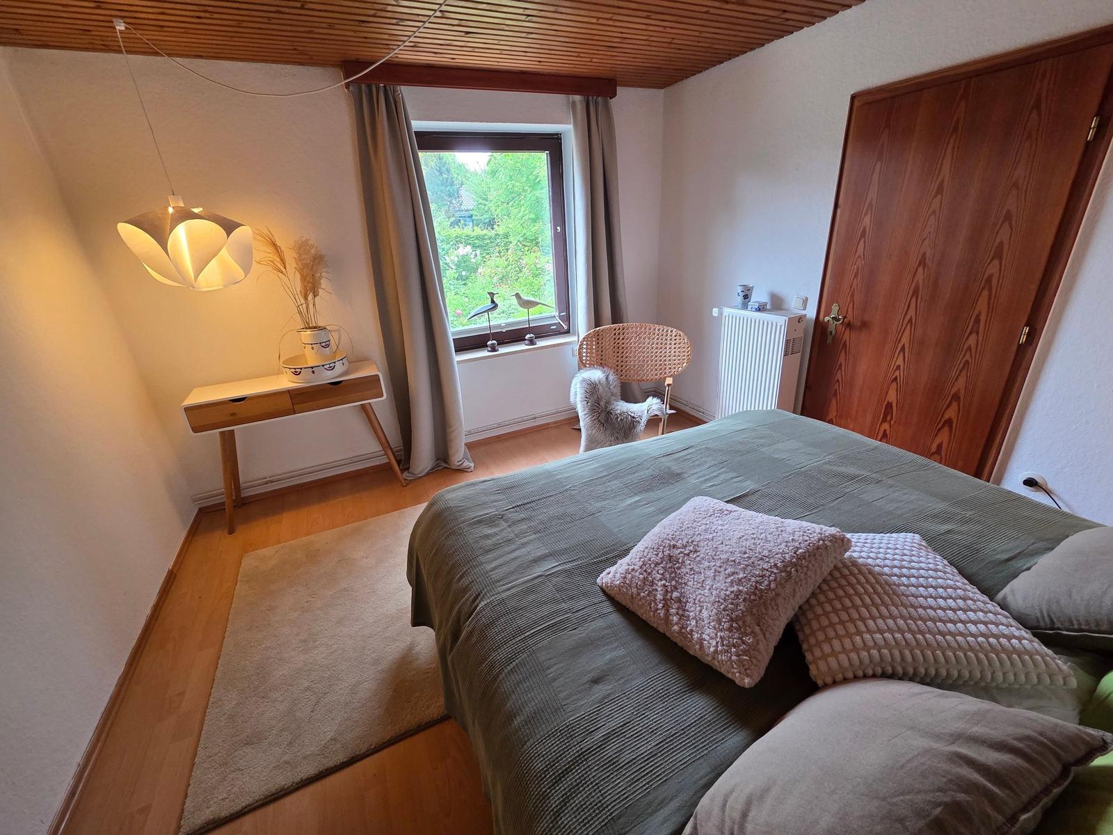 Schlafzimmer mit Bett, Fenster, Stuhl und Schreibtisch.