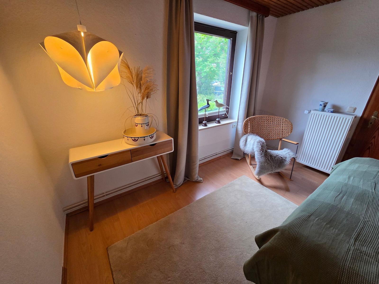 Schlafzimmer mit Bett, Schreibtisch, Stuhl und Fenster. Decke aus Holz.