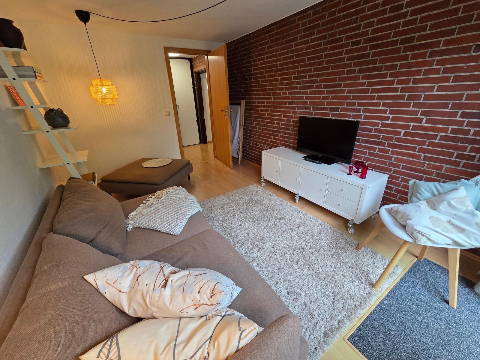 Wohnzimmer mit Sofa, Fernseher und Backsteinwand.