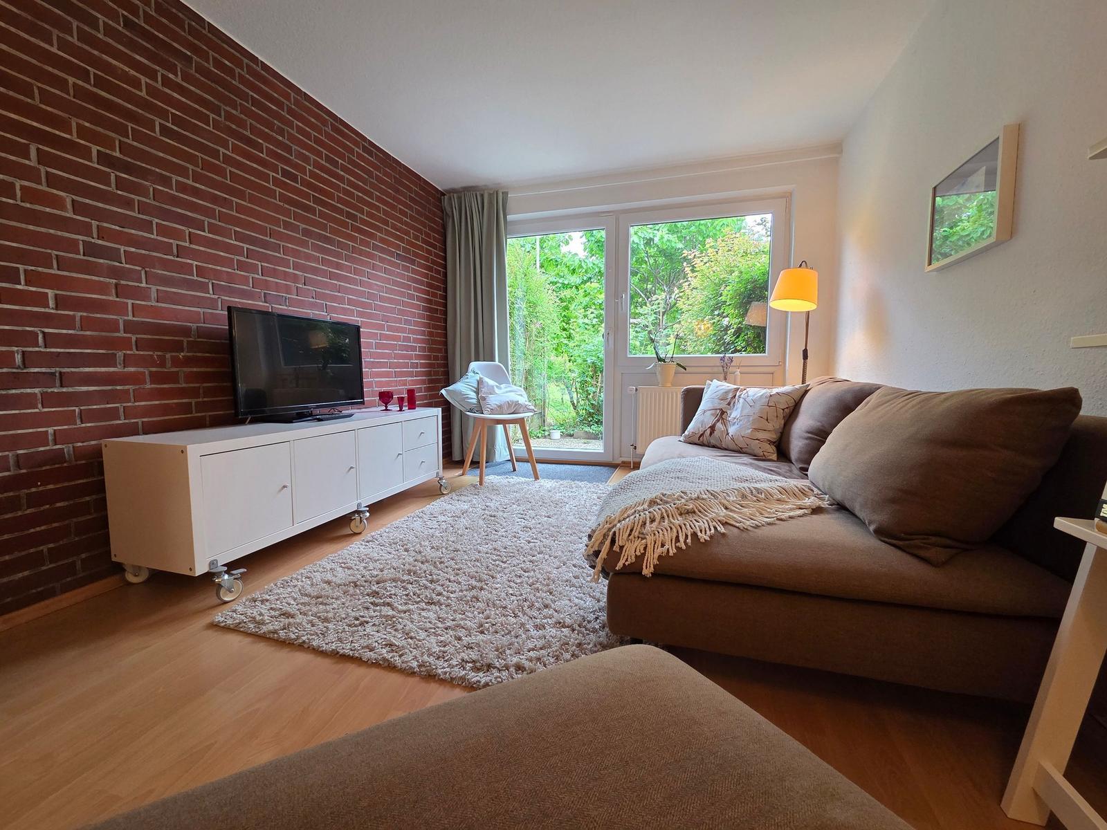 Wohnzimmer mit Sofa, Fernseher und Blick auf Garten