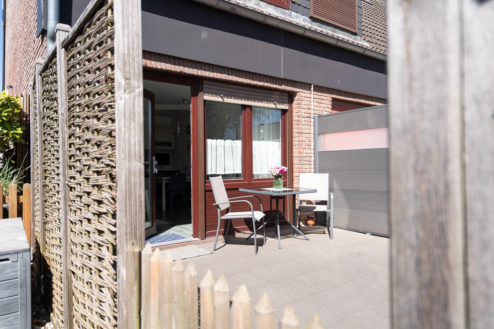 Terrasse mit Tisch und zwei Stühlen vor einer Haustür mit Blick ins Haus.