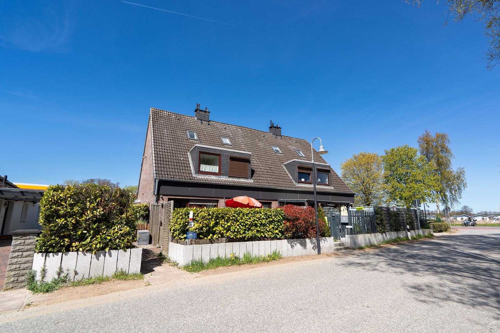 Ein zweistöckiges Haus mit Dachfenstern und einer grünen Hecke vor dem Eingang.