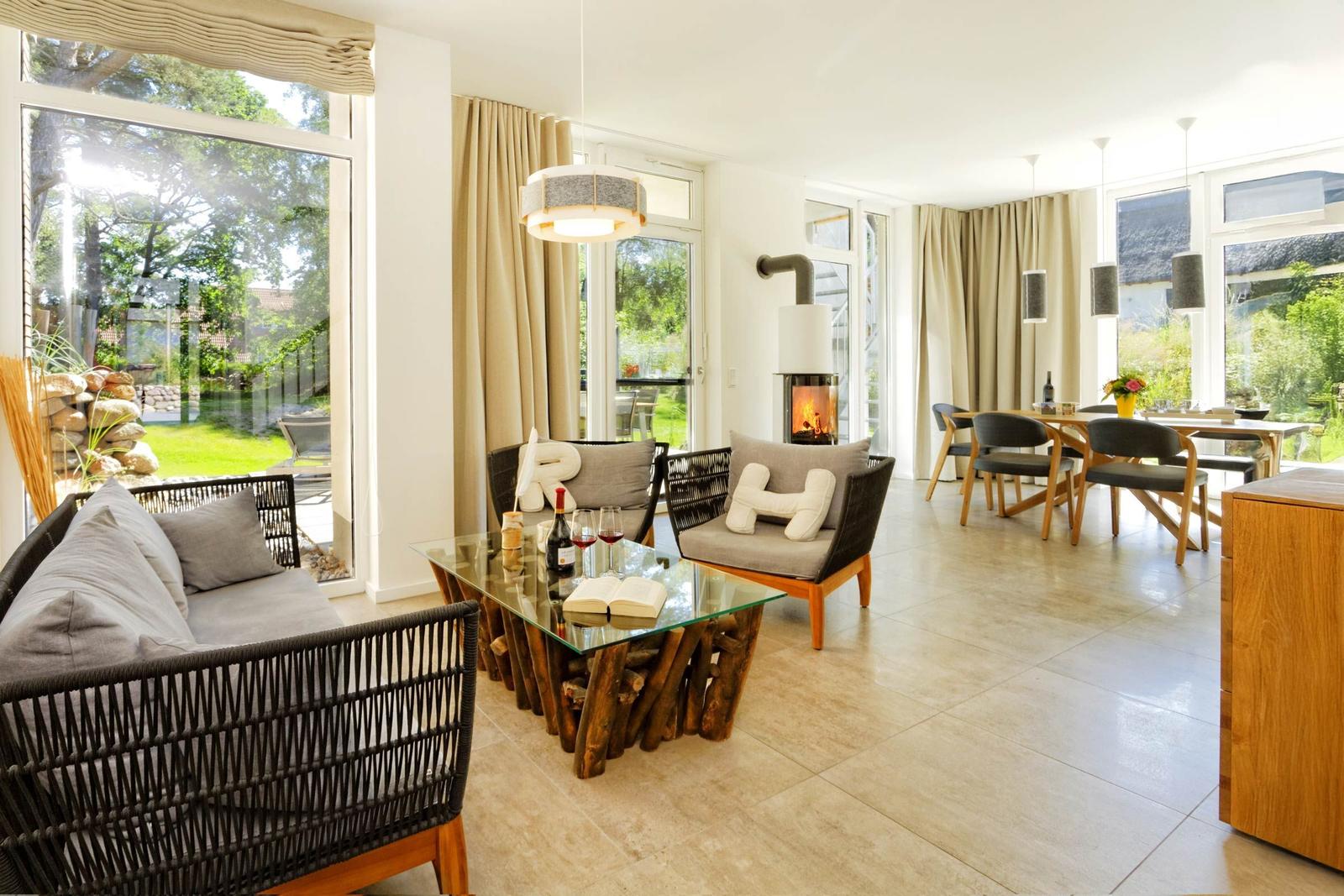 Wohn- und Essbereich mit Kamin, Glas-Tisch und Sitzgelegenheiten. Große Fenster mit Blick auf Garten.