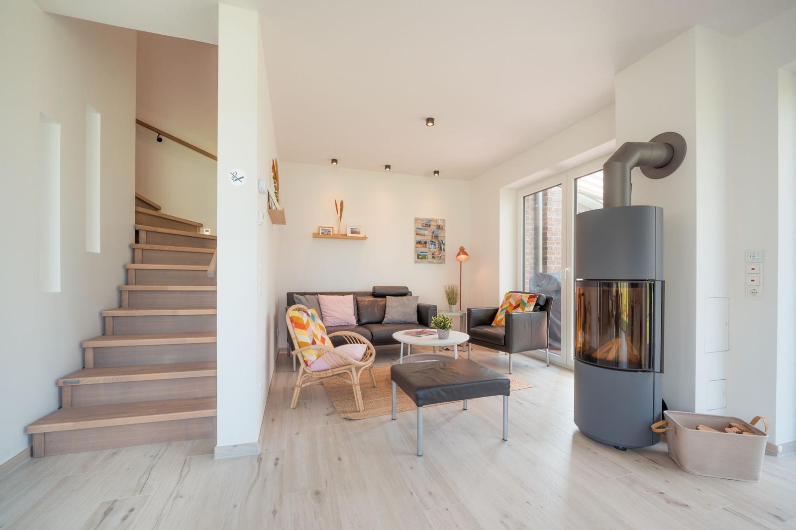 Wohnbereich mit Sofa, Sitzgelegenheiten und Kaminofen. Holztreppe führt zur oberen Etage.