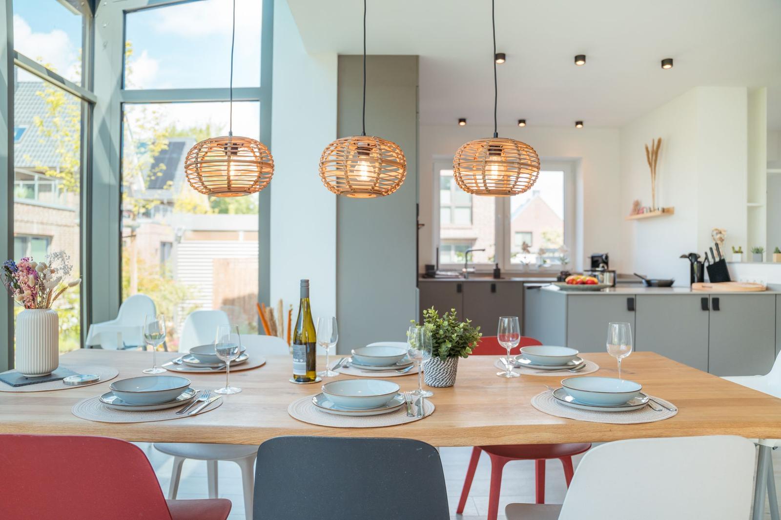 Esszimmer mit Holztisch, Stühlen und drei hängenden Lampen. Küche im Hintergrund.
