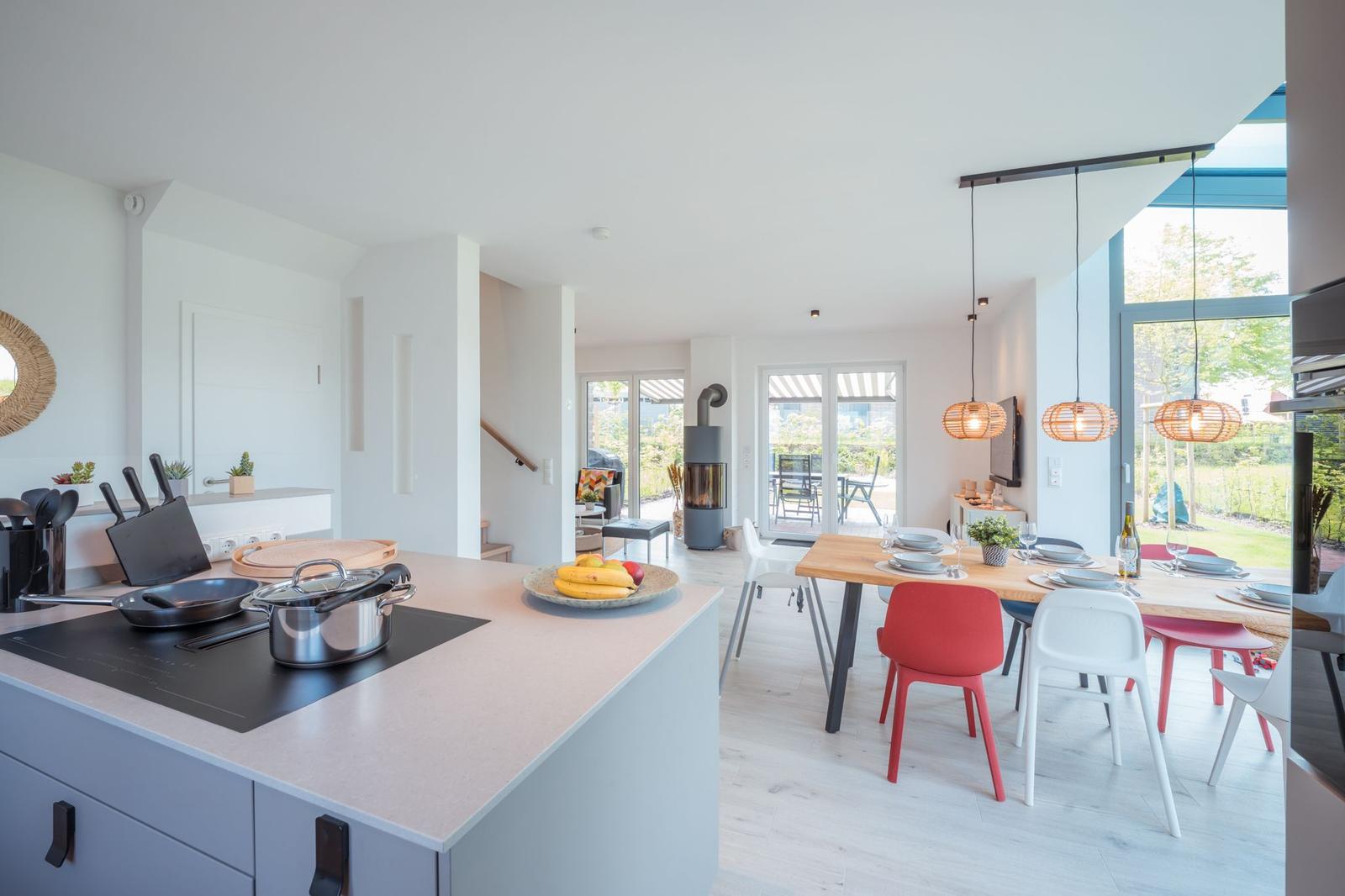 Moderne Küche mit Essbereich, Holztisch und bunten Stühlen. Blick auf Garten durch Glasfront.