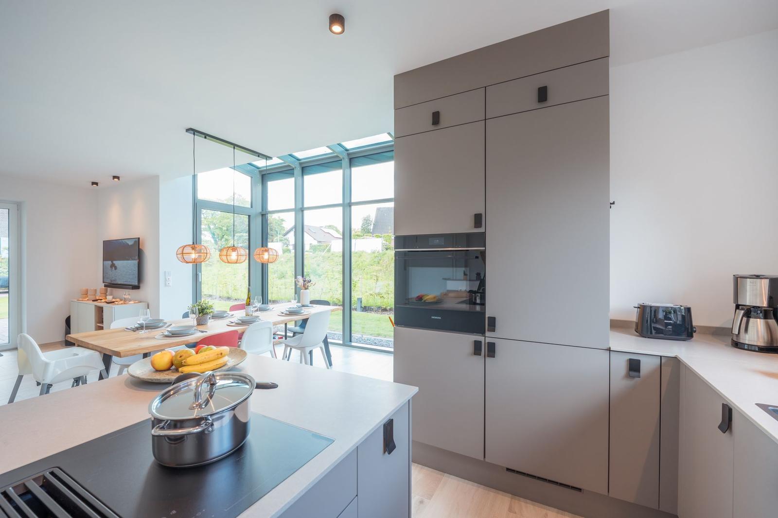 Moderne Küche mit Essbereich und großem Fenster. Küchenspüle, Herd und Einbauofen sichtbar.