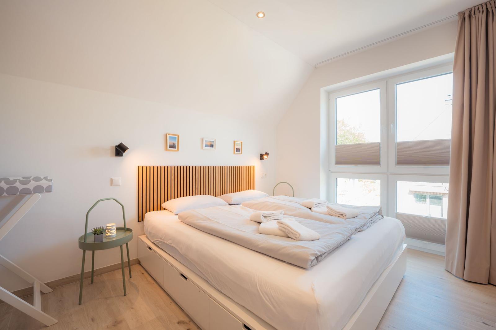 Schlafzimmer mit Doppelbett, Holzkopfteil und großem Fenster mit Blick nach draußen.