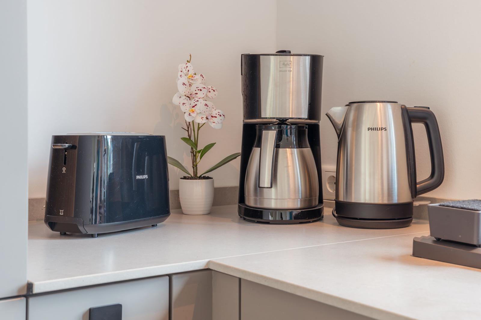 Küchenzeile mit Toaster, Kaffeemaschine und Wasserkocher sowie einer Pflanze.