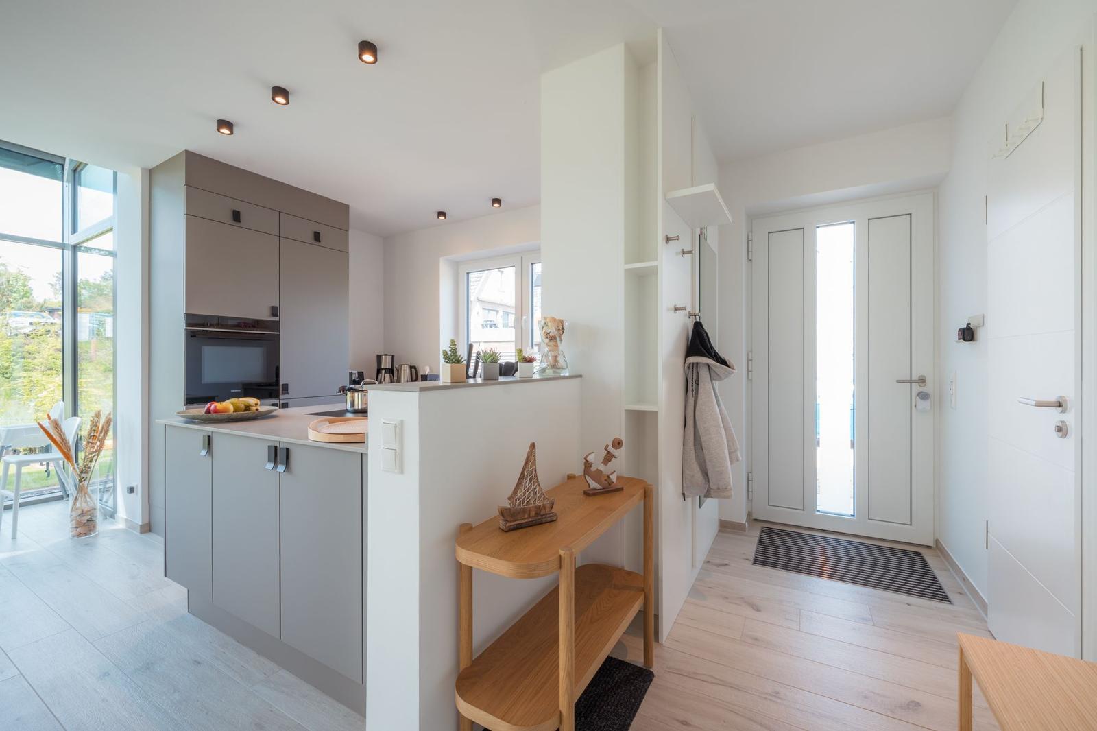 Küche mit Arbeitsplatte, integriertem Ofen und Fenster. Flur mit Garderobe und Holzbank.