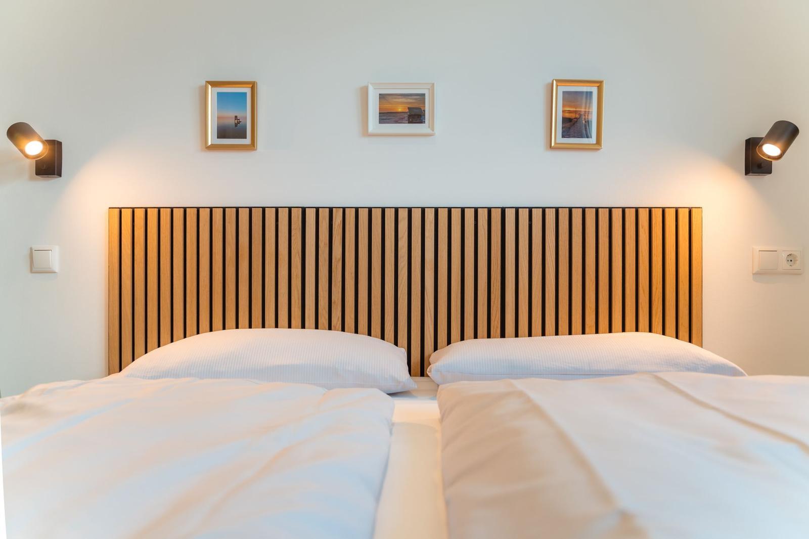 Doppelbett mit Holz-Kopfteil und drei Wandbildern über dem Bett.