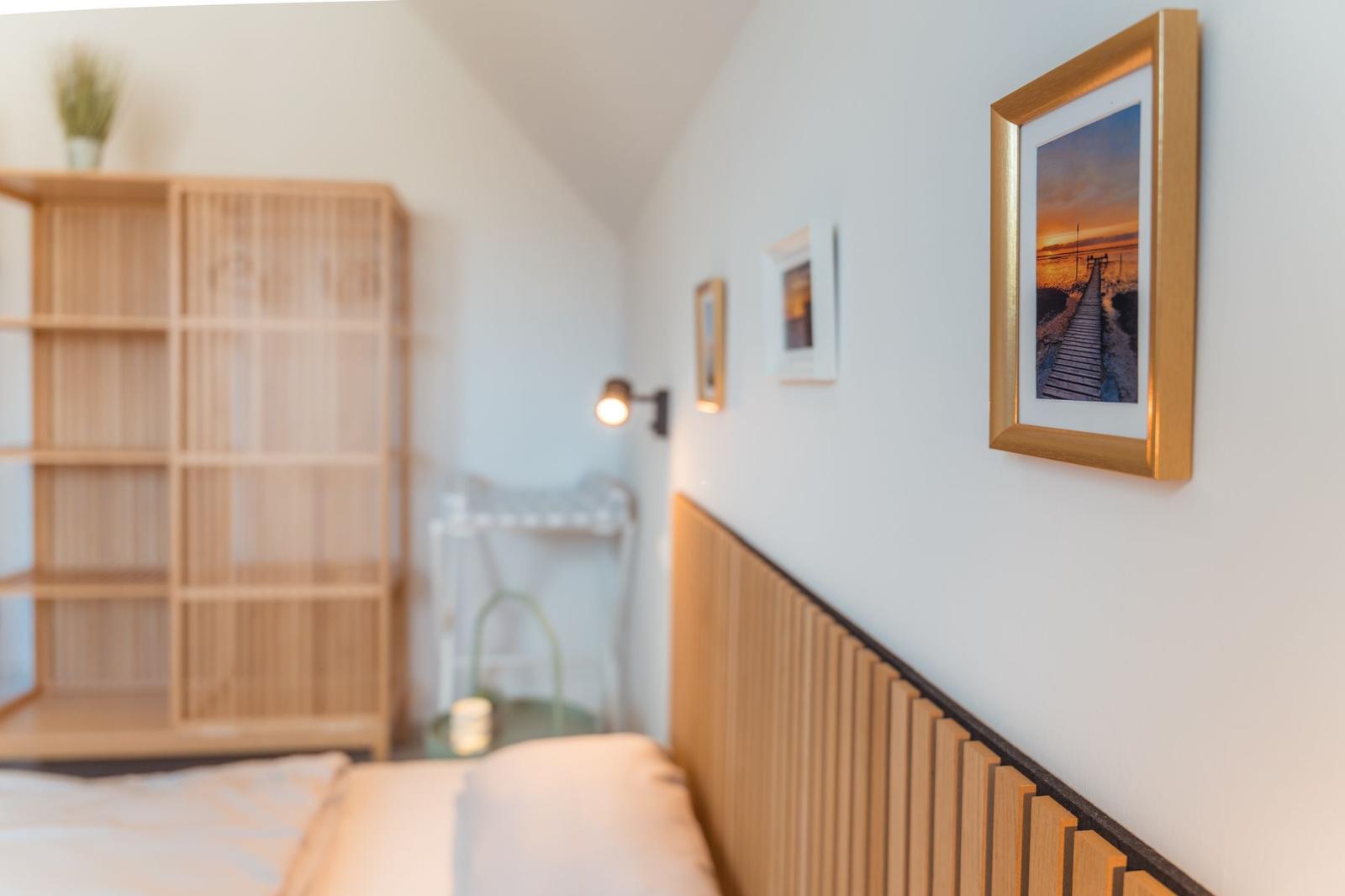 Schlafzimmer mit Holzbett, Wandregal und Bildern an der Wand.