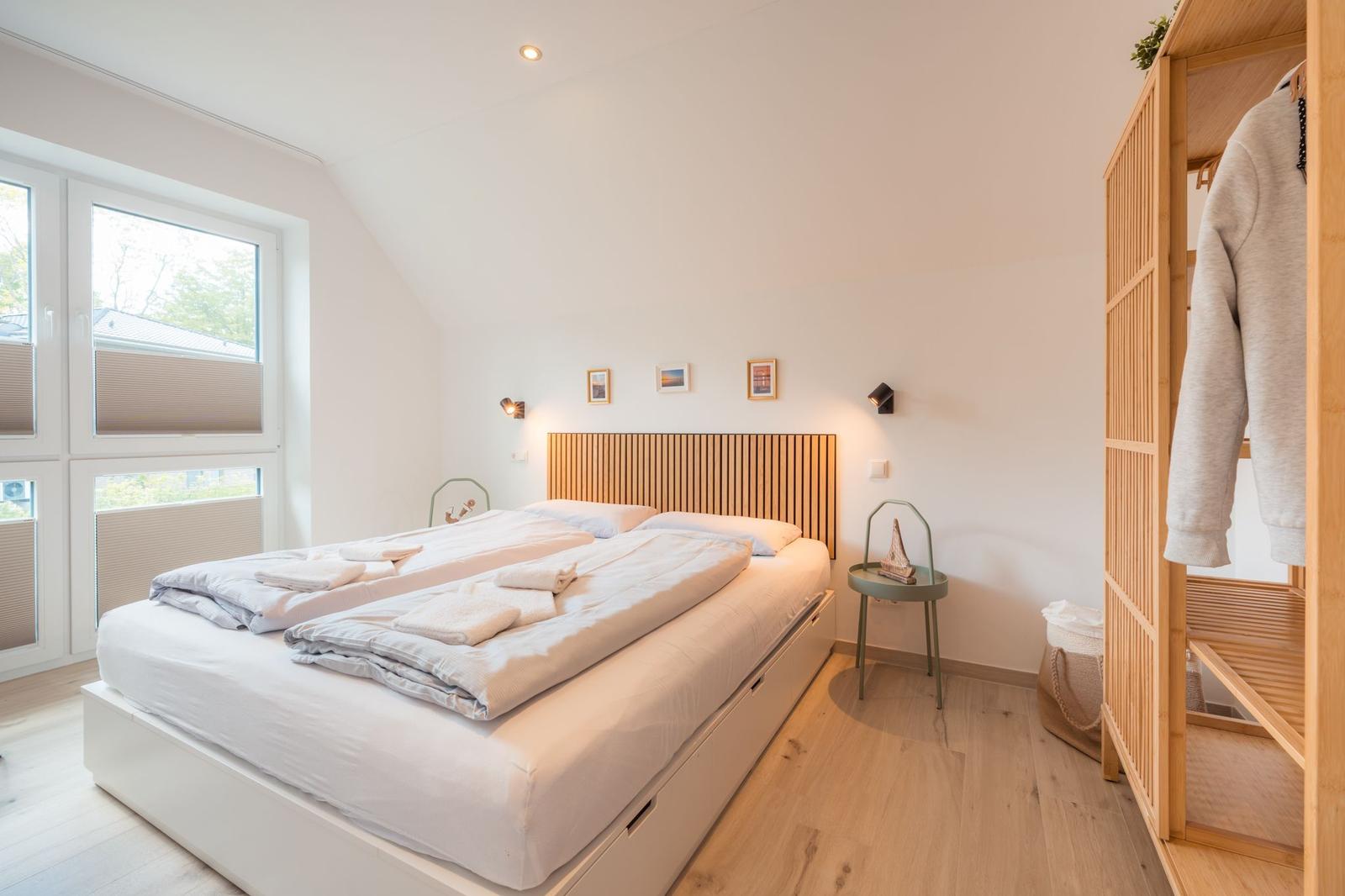 Schlafzimmer mit Doppelbett, Holzmöbel und großem Fenster. Kleine Nachttischlampe und Kleiderständer.