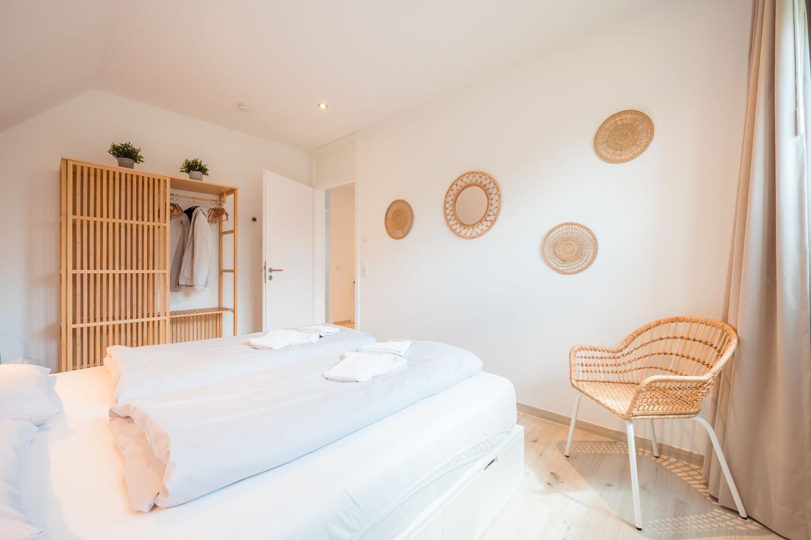 Schlafzimmer mit Doppelbett, Kleiderschrank und Stuhl. Wanddekoration aus geflochtenen Runden.
