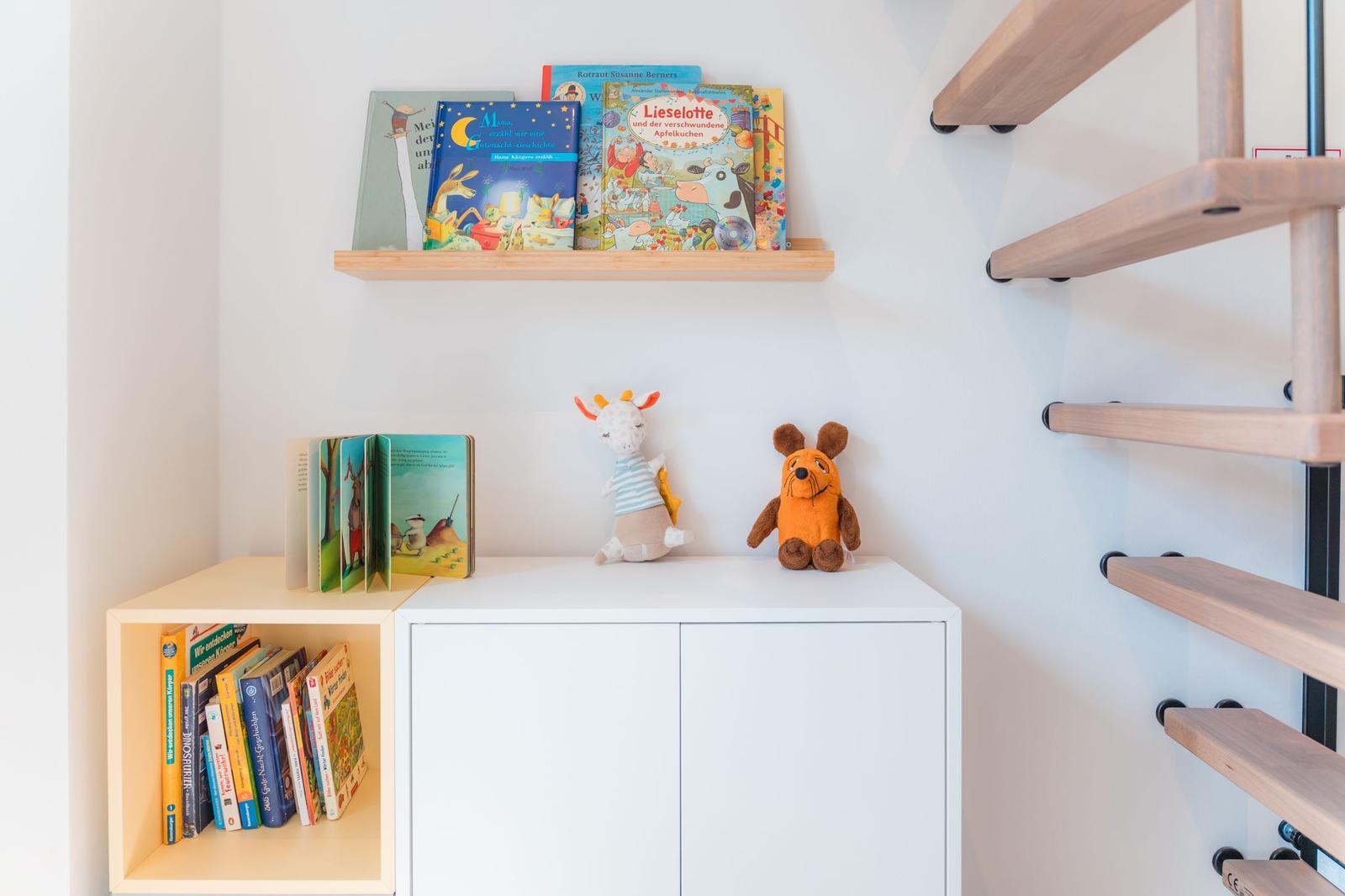 Bücherregal mit Kinderbüchern und Stofftieren neben einer Holztreppe.