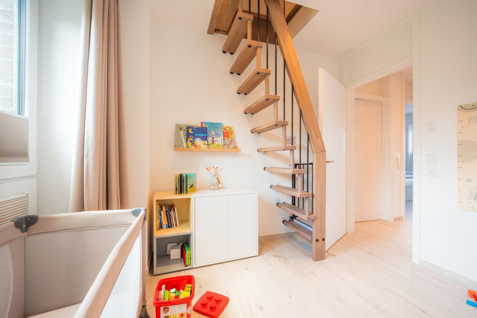 Kinderzimmer mit Spielzeug, Bücherregal und Holztreppe.