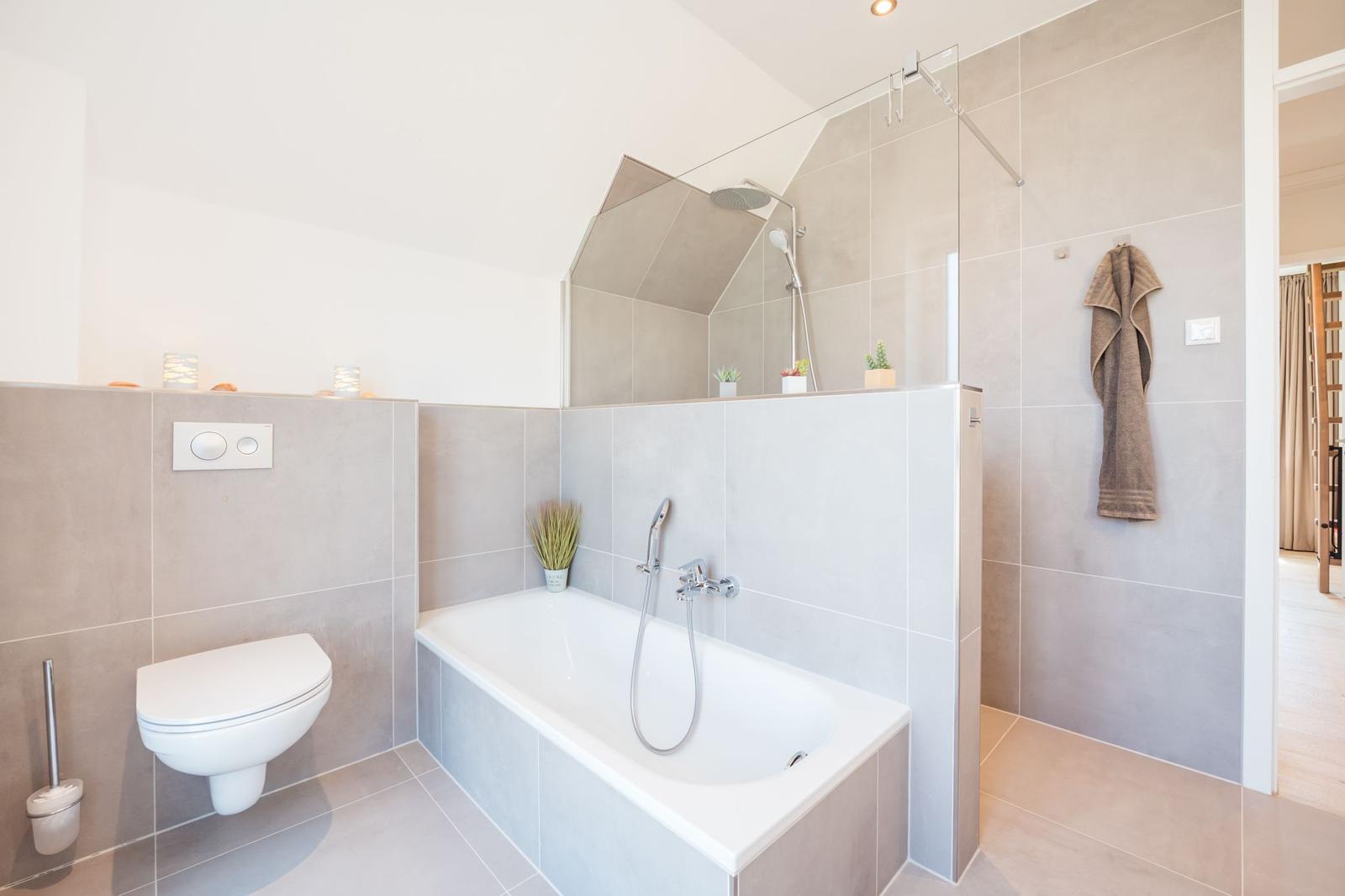 Bad mit Badewanne, Dusche und Toilette. Wandfliesen und Handtuch.