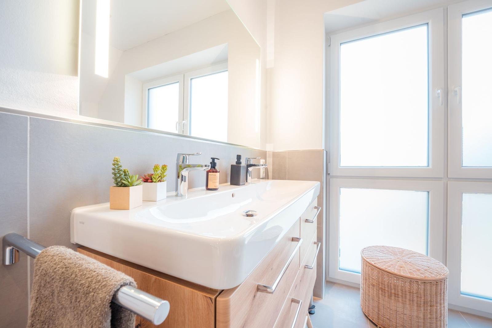 Badezimmer mit Waschbecken, Spiegel, Fenster und Wickerhocker.