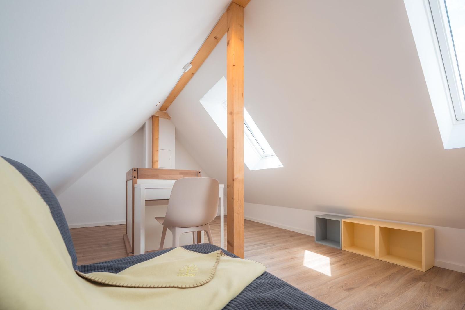 Dachgeschosszimmer mit Schreibtisch, Bett und Fenstern.