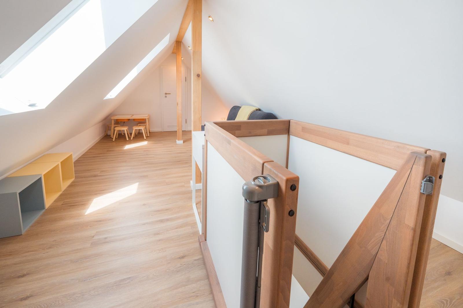 Dachgeschosszimmer mit Holzboden, Babygitter, Tisch und Stühlen sowie Dachfenstern.