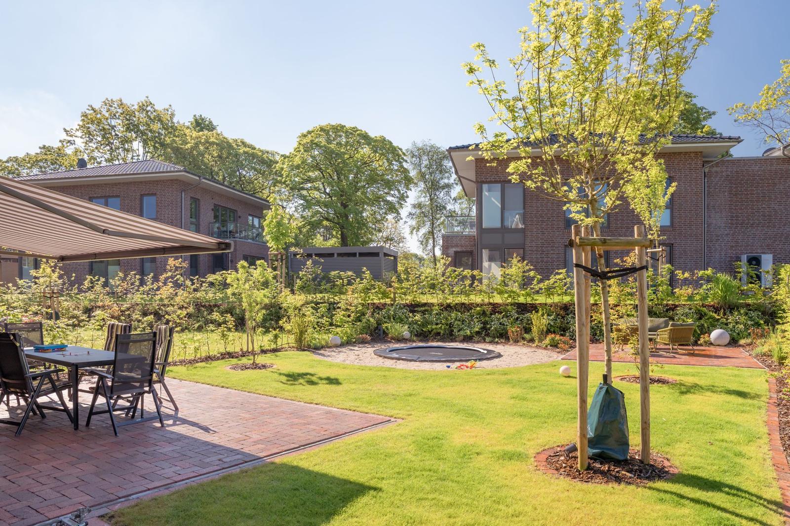 Hinterhof mit Grillplatz, Trampolin und Sitzgelegenheiten. Grünflächen und Bäume umgeben die Terrasse.