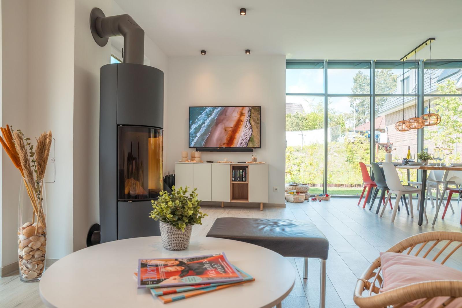 Wohnzimmer mit Kamin, Fernseher und großem Fenster zur Terrasse.