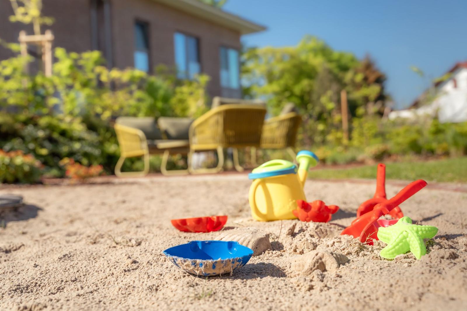 Sandkasten mit bunten Spielzeugen vor einer Terrasse mit Sitzgelegenheiten.