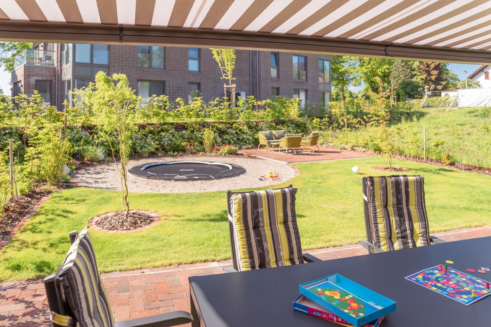 Terrasse mit Sitzgruppe, Tisch, Trampolin und Garten.