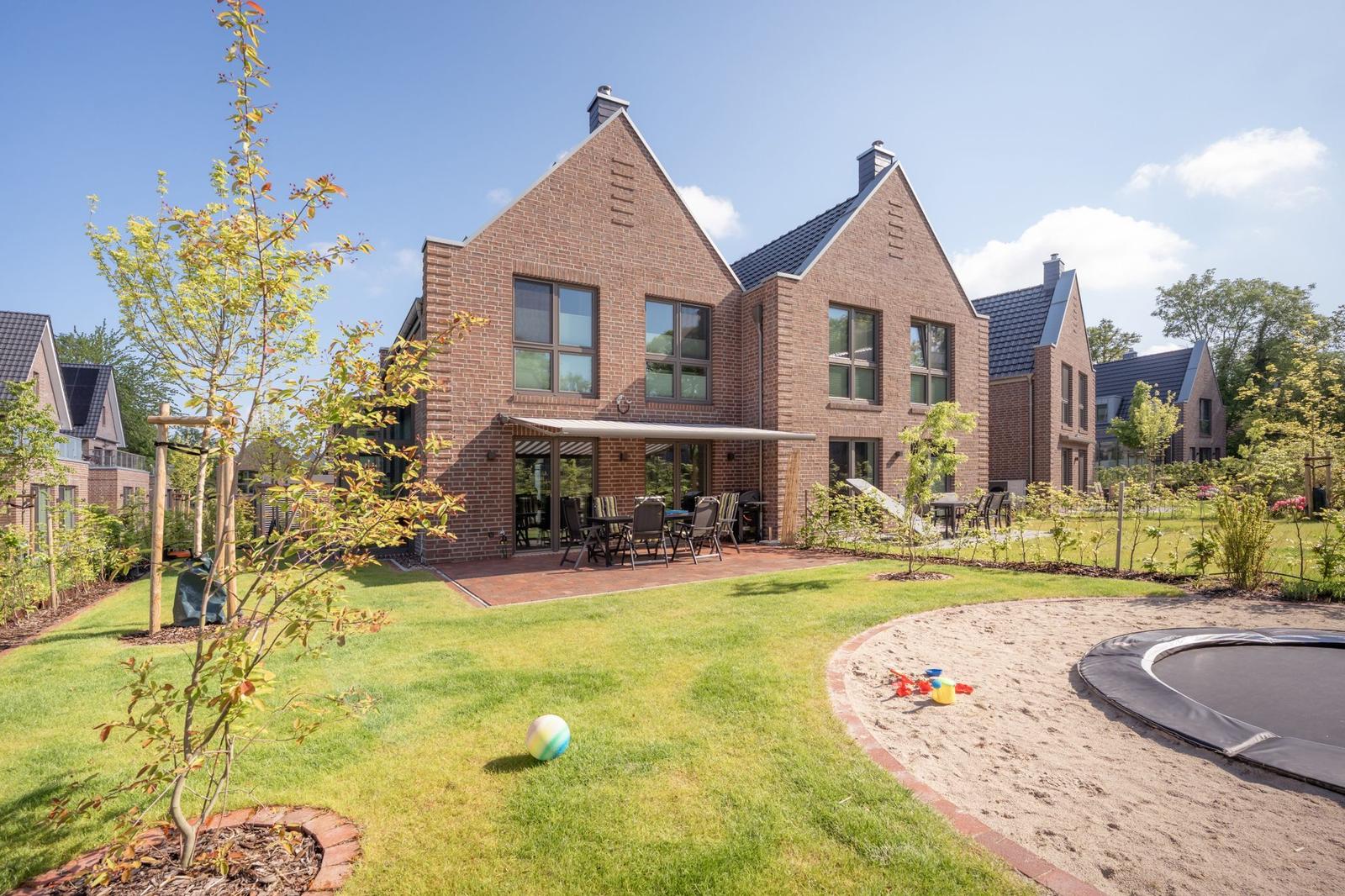 Haus mit Garten, Terrasse und Trampolin. Spielplatz und grüner Rasenbereich.