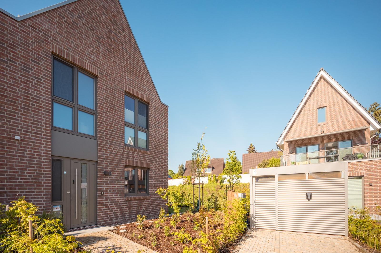Zwei moderne Backsteinhäuser mit Garten und Garage unter blauem Himmel.
