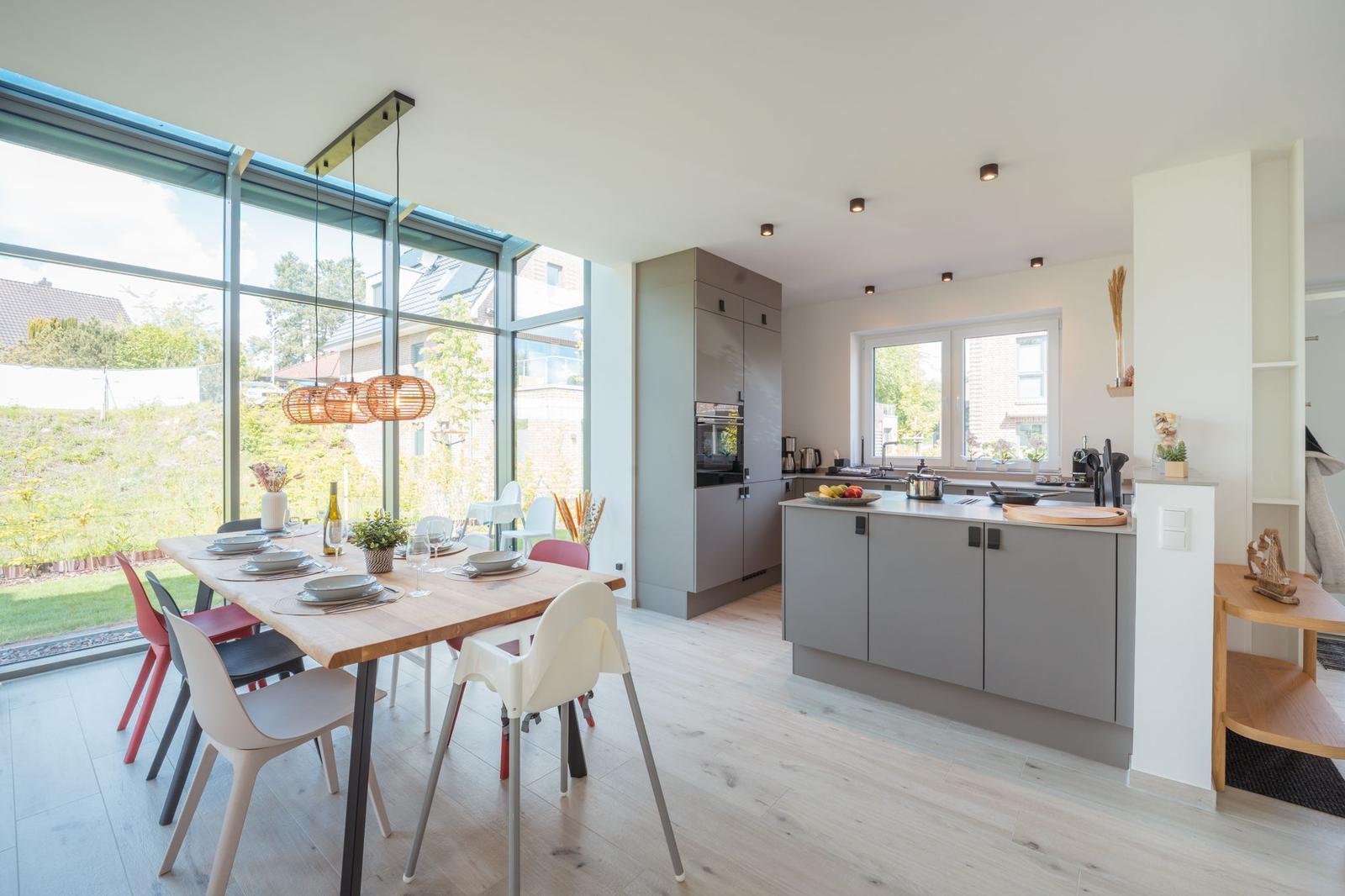 Moderne Küche mit Essbereich und großem Fenster. Holzfußboden und graue Schränke.