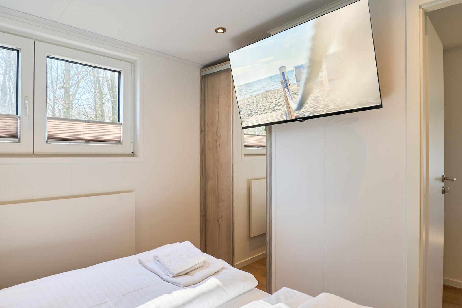 Schlafzimmer mit Bett, Fernseher und Fenster mit Blick auf Bäume.