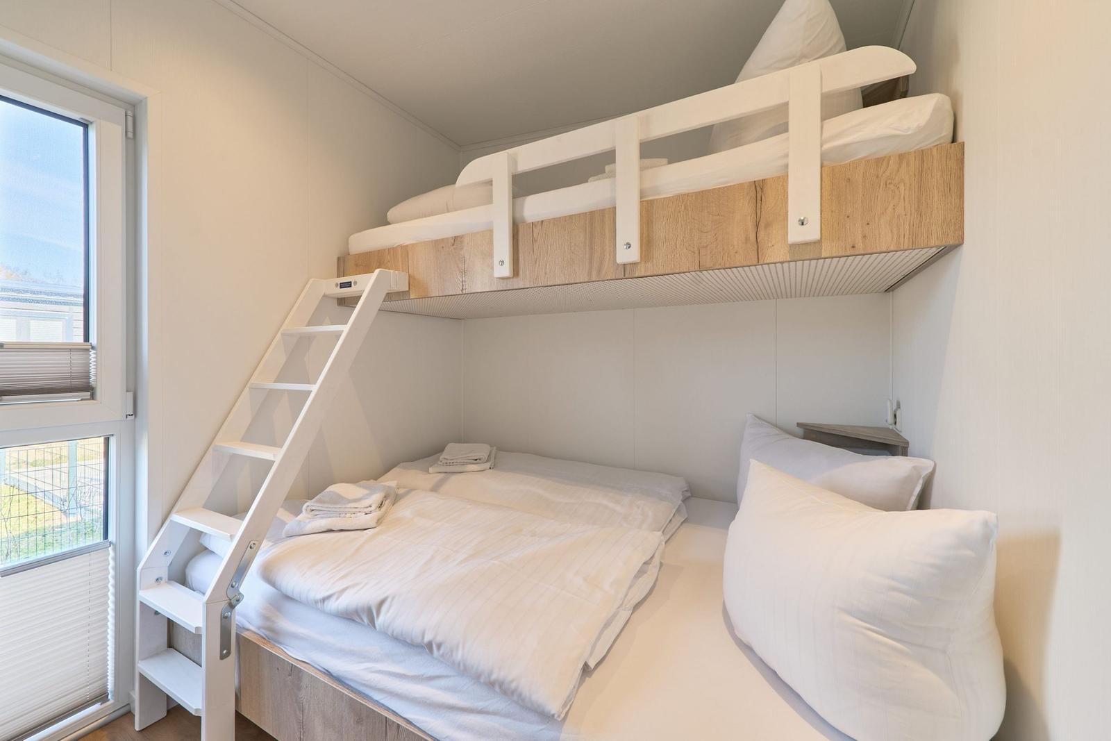 Zimmer mit Doppelbett und oberem Schlafplatz mit Leiter und Fenster.