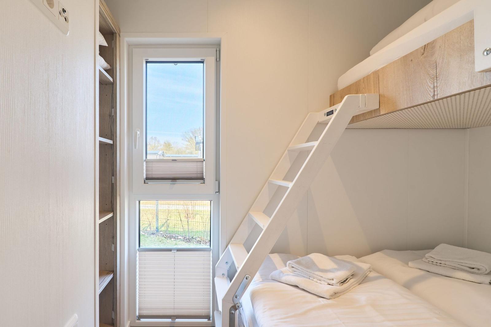Zimmer mit Doppelstockbett, Fenster und Kleiderschrank.