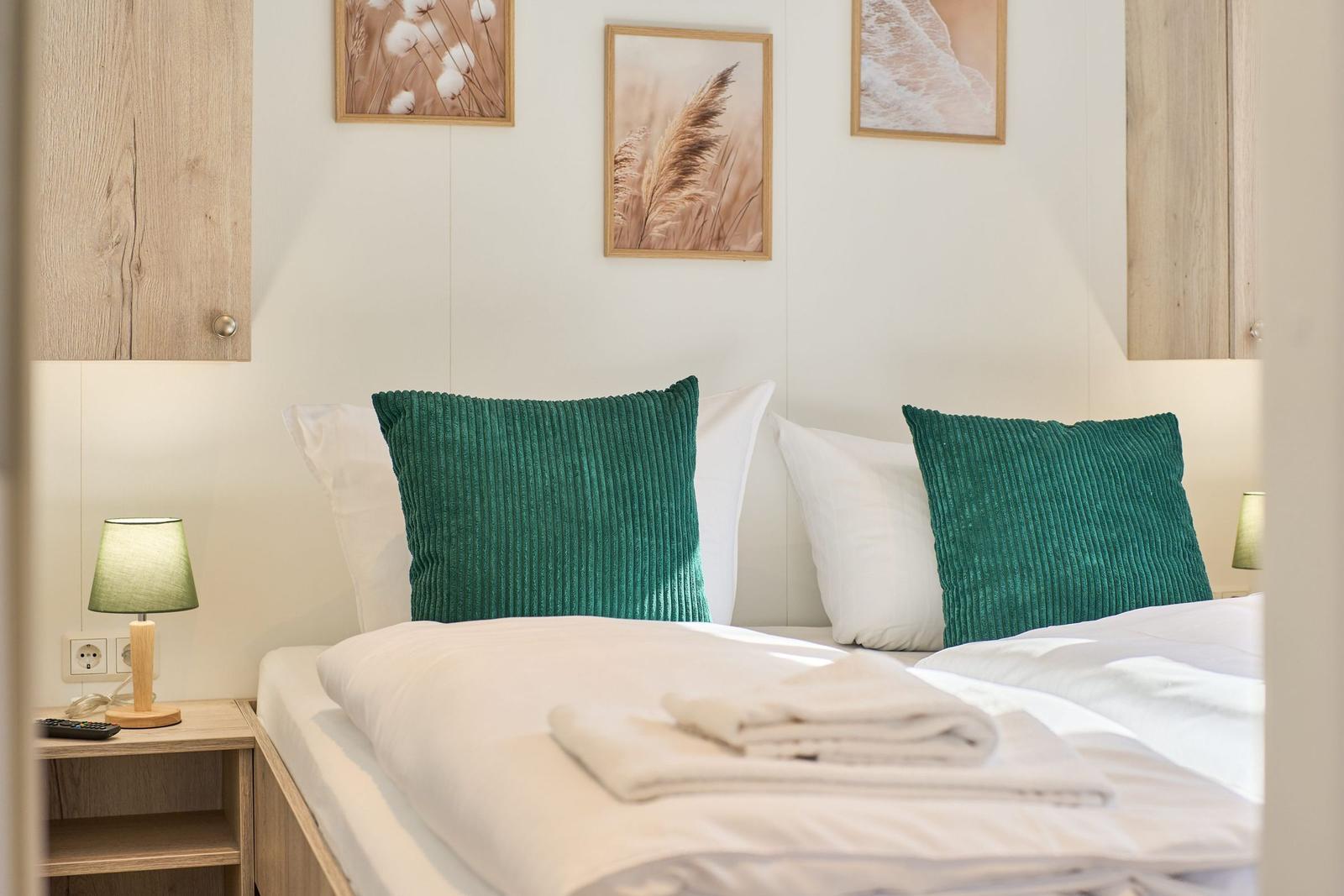 Schlafzimmer mit Bett, grünen Kissen und Wandbildern.