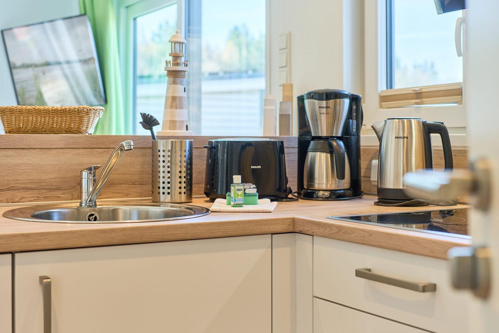 Küche mit Spüle, Toaster, Kaffeemaschine und Wasserkocher auf Holzoberfläche.
