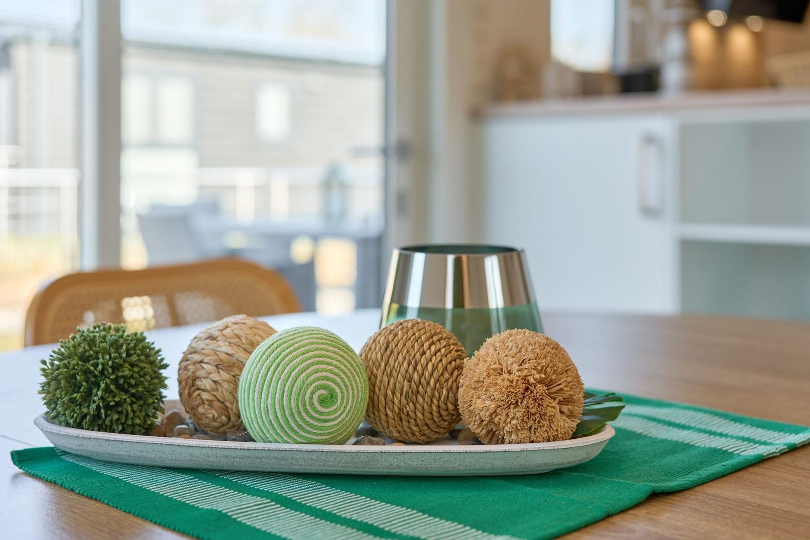 Tischdekoration mit grünem Teller, Kugeln und Glas auf Holztisch