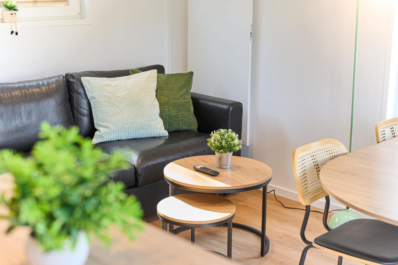 Schwarzes Sofa mit Kissen, runder Tisch und Stühle im Wohn- und Essbereich.