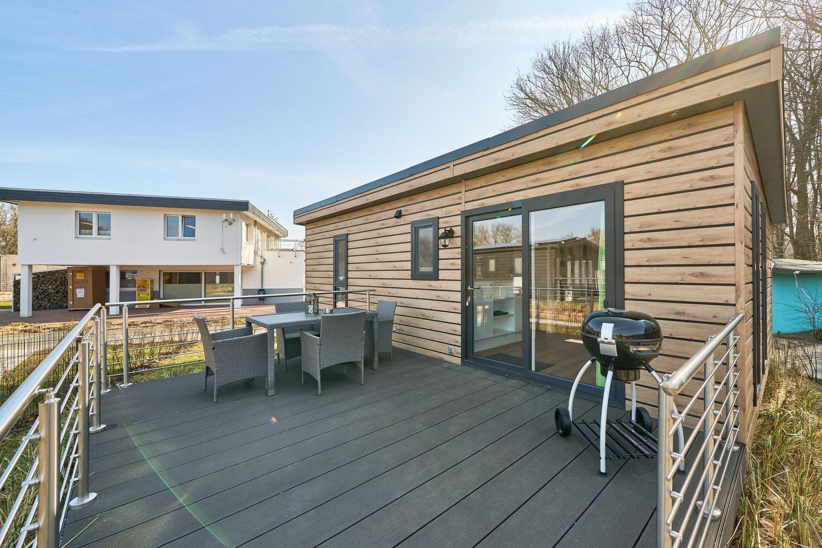 Terrasse mit Tisch, Stühlen und Grill vor einem Holzhaus mit Glasfront.