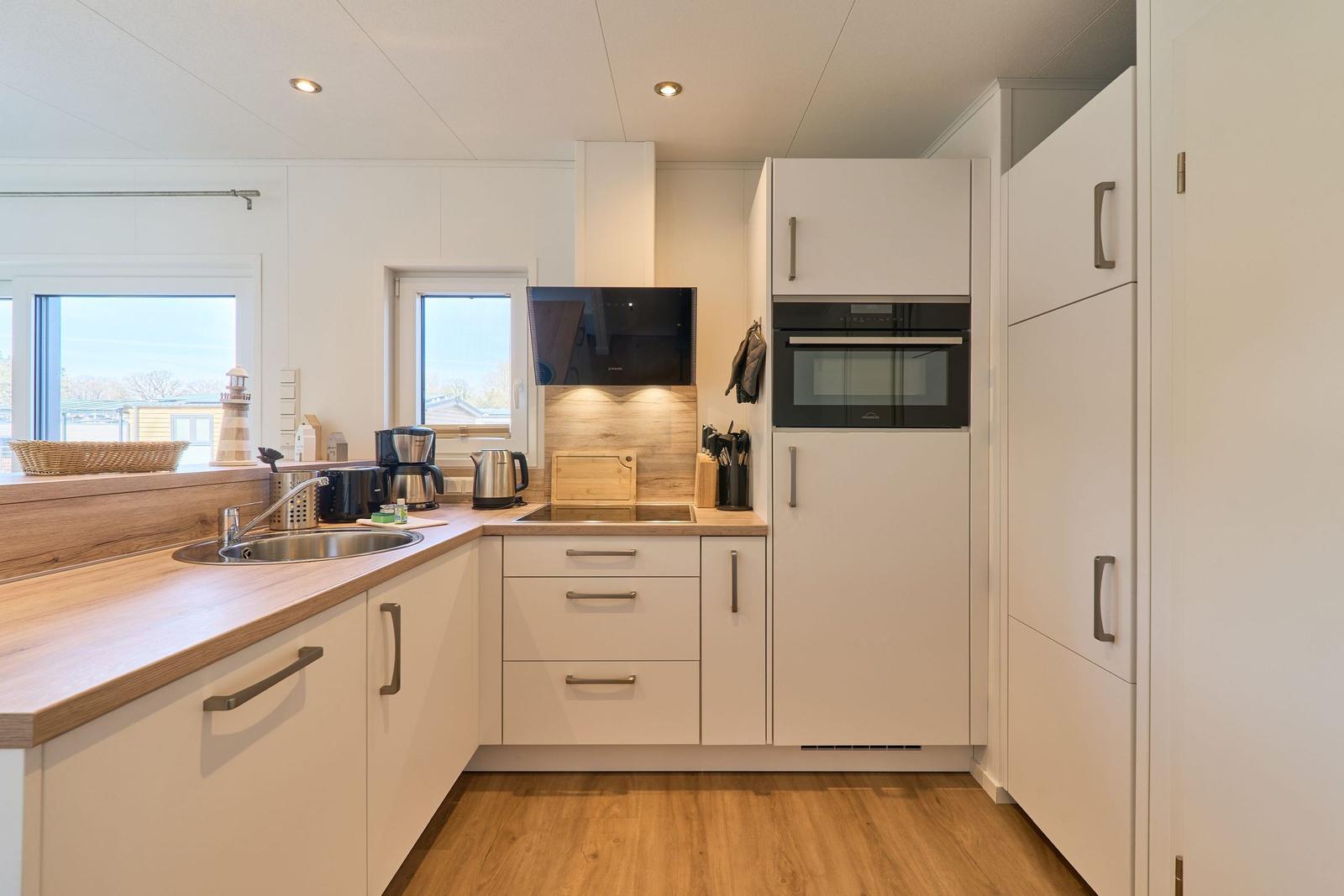 Moderne Küche mit weißen Schränken, Holzoberfläche und integriertem Backofen.