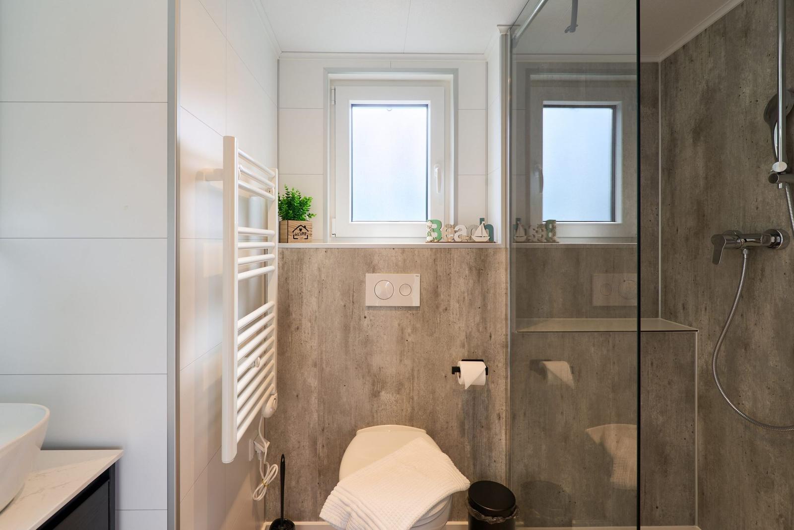 Badezimmer mit Dusche, Toilette und Fenster. Wandverkleidung aus Betonoptik.