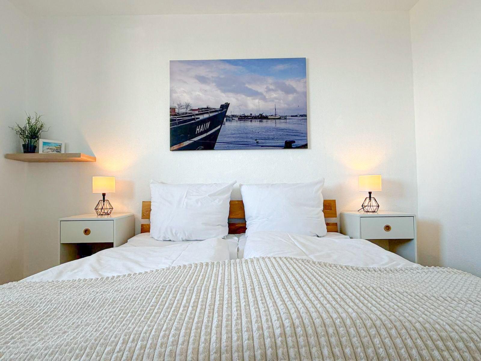Schlafzimmer mit Bett, Nachttischen und Wandbild von Booten.