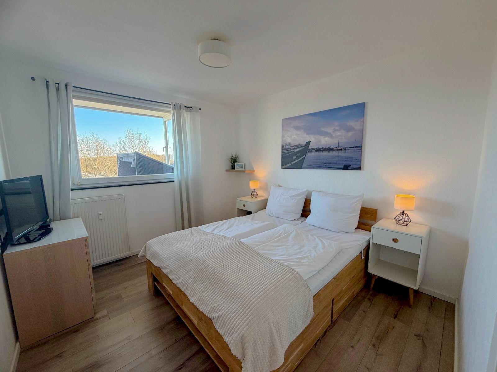 Schlafzimmer mit Doppelbett, zwei Nachttischen und Fernseher. Fenster mit Blick nach draußen.